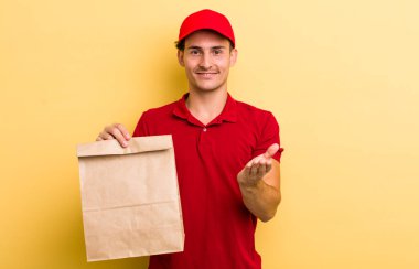 Genç yakışıklı adam mutlu bir şekilde gülümsüyor ve bir konsept sunuyor. teslimat ve paket konsepti