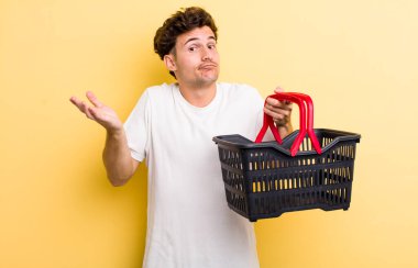 Genç yakışıklı adam şaşkın, şaşkın ve şüpheci hissediyor. boş alışveriş sepeti kavramı