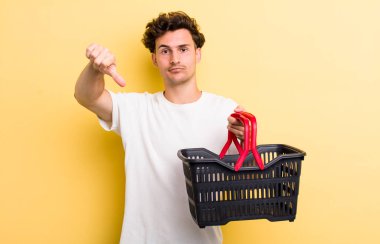 Genç ve yakışıklı adam kendini kötü hissediyor, baş parmağını kaldırıyor. boş alışveriş sepeti kavramı