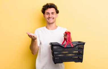 Genç yakışıklı adam mutlu bir şekilde gülümsüyor ve bir konsept sunuyor. boş alışveriş sepeti kavramı