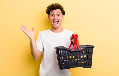 Genç yakışıklı adam kendini mutlu hissediyor ve inanılmaz bir şeye hayret ediyor. boş alışveriş sepeti kavramı