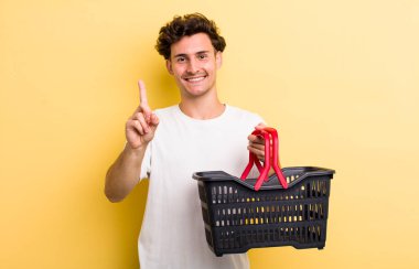 Genç yakışıklı adam gururla gülümsüyor ve kendinden emin bir numara oluyor. boş alışveriş sepeti kavramı