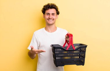 Genç yakışıklı adam neşeyle gülümsüyor, mutlu hissediyor ve bir konsept gösteriyor. boş alışveriş sepeti kavramı