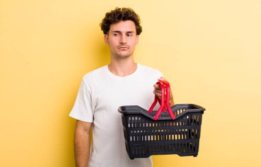 Genç yakışıklı adam üzgün, üzgün ya da kızgın hissediyor ve yana bakıyor. boş alışveriş sepeti kavramı