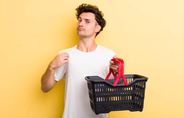 Genç yakışıklı adam kibirli, başarılı, pozitif ve gururlu görünüyor. boş alışveriş sepeti kavramı