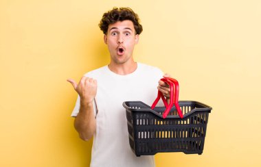 Genç ve yakışıklı bir adam inançsızlığa şaşırmış görünüyor. boş alışveriş sepeti kavramı