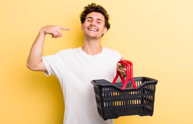 Genç ve yakışıklı adam, kendine güvenerek gülümsüyor. boş alışveriş sepeti kavramı