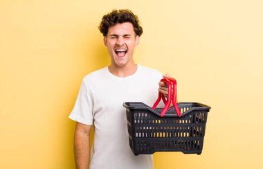 Genç yakışıklı adam agresif bir şekilde bağırıyor, çok kızgın görünüyor. boş alışveriş sepeti kavramı