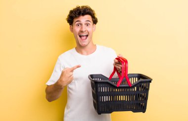 Genç yakışıklı adam heyecanlı ve şaşırmış görünüyor. boş alışveriş sepeti kavramı