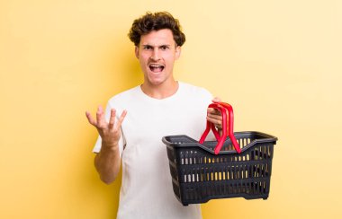 Genç ve yakışıklı adam sinirli, sinirli ve sinirli görünüyor. boş alışveriş sepeti kavramı