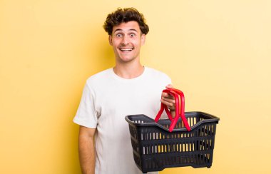 Genç yakışıklı adam mutlu ve hoş bir şekilde şaşırmış görünüyor. boş alışveriş sepeti kavramı