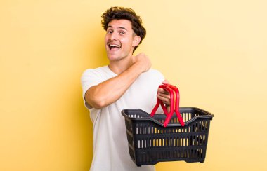 Genç yakışıklı adam kendini mutlu hissediyor ve bir meydan okumayla yüzleşiyor ya da kutluyor. boş alışveriş sepeti kavramı