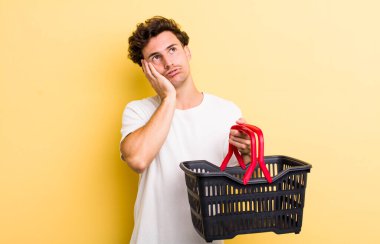 Genç ve yakışıklı bir adam bıkkın, yorgun ve uykulu hissediyor. boş alışveriş sepeti kavramı