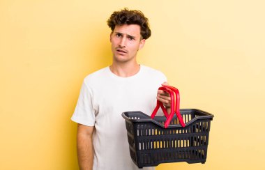 Genç yakışıklı adam şaşkın ve şaşkın hissediyor. boş alışveriş sepeti kavramı