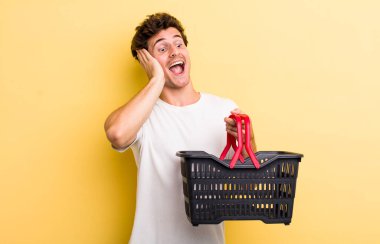 Genç yakışıklı adam mutlu, heyecanlı ve şaşırmış hissediyor. boş alışveriş sepeti kavramı