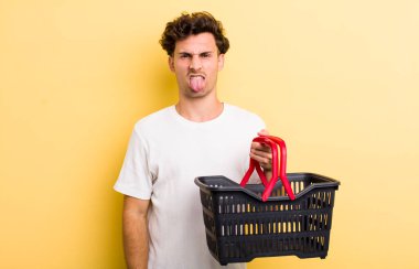 Genç yakışıklı adam iğreniyor, sinirleniyor ve dilini çıkarıyor. boş alışveriş sepeti kavramı