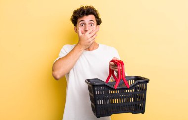 Genç ve yakışıklı adam elleri ile ağzını kapatıyor ve şoka giriyor. boş alışveriş sepeti kavramı