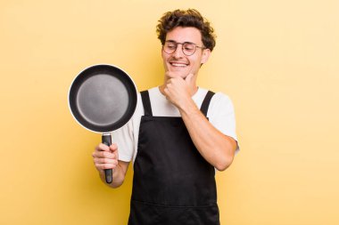 Genç, yakışıklı, mutlu, kendine güvenen ve elleri çenesinde gülümseyen adam. Şefin tava konsepti.