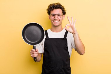 Genç yakışıklı adam kendini mutlu hissediyor, iyi bir jestle onaylıyor. Şefin tava konsepti.
