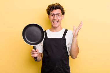 Genç yakışıklı adam kendini mutlu hissediyor ve inanılmaz bir şeye hayret ediyor. Şefin tava konsepti.