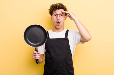 Genç yakışıklı adam mutlu, şaşkın ve şaşırmış görünüyor. Şefin tava konsepti.