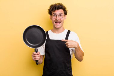 Genç yakışıklı adam kendini mutlu hissediyor ve heyecanla kendini işaret ediyor. Şefin tava konsepti.