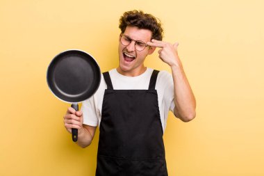 Genç yakışıklı adam mutsuz ve stresli görünüyor, intihar jesti silah işareti yapıyor. Şefin tava konsepti.