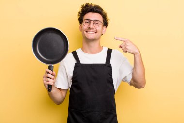 Genç ve yakışıklı adam, kendine güvenerek gülümsüyor. Şefin tava konsepti.