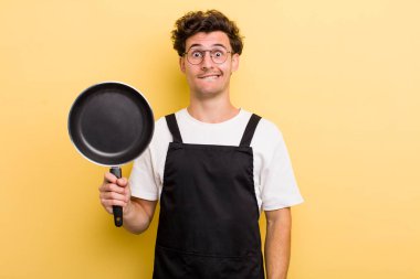 Genç ve yakışıklı adam kafası karışmış ve şaşkın görünüyor. Şefin tava konsepti.