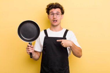 Şok olmuş ve ağzı açık, kendini işaret eden genç ve yakışıklı bir adam. Şefin tava konsepti.