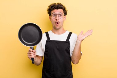 Genç, yakışıklı adam şaşırmış ve şok olmuş görünüyor. Çenesi düşmüş, elinde bir nesne var. Şefin tava konsepti.