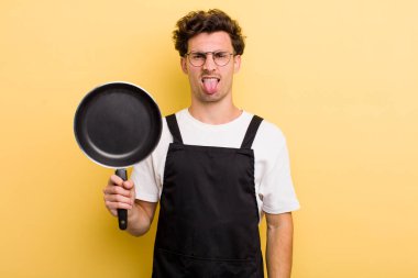 Genç yakışıklı adam iğreniyor, sinirleniyor ve dilini çıkarıyor. Şefin tava konsepti.