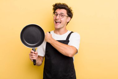 Genç yakışıklı adam kendini mutlu hissediyor ve bir meydan okumayla yüzleşiyor ya da kutluyor. Şefin tava konsepti.