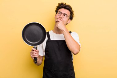 Genç yakışıklı adam düşünüyor, kuşkulu ve şaşkın hissediyor. Şefin tava konsepti.