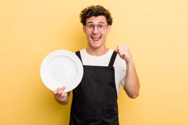 Genç yakışıklı adam şok olmuş hissediyor, gülüyor ve başarıyı kutluyor. boş tabak kavramı