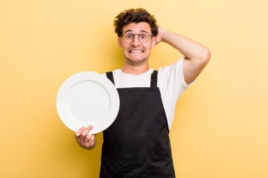 Genç ve yakışıklı adam stresli, endişeli ya da korkmuş, elleri başının üstünde. boş tabak kavramı