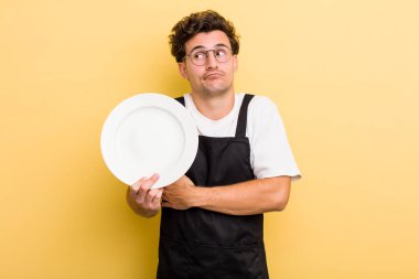 Genç yakışıklı adam omuz silkiyor, kafası karışık ve kararsız hissediyor. boş tabak kavramı