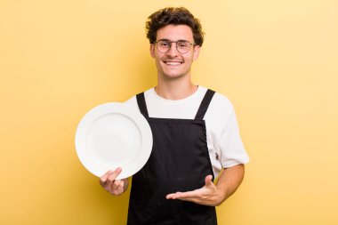 Genç yakışıklı adam neşeyle gülümsüyor, mutlu hissediyor ve bir konsept gösteriyor. boş tabak kavramı