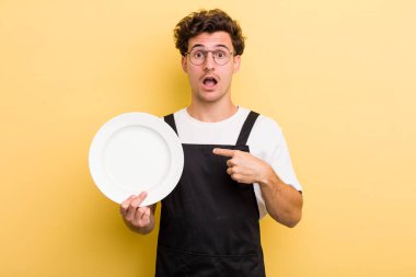 Şok olmuş ve ağzı açık, kendini işaret eden genç ve yakışıklı bir adam. boş tabak kavramı