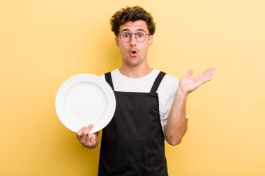 Genç, yakışıklı adam şaşırmış ve şok olmuş görünüyor. Çenesi düşmüş, elinde bir nesne var. boş tabak kavramı