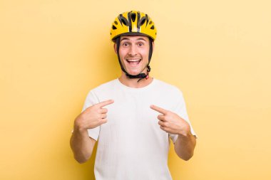 Genç yakışıklı adam kendini mutlu hissediyor ve heyecanla kendini işaret ediyor. Bisiklet konsepti motor konsepti