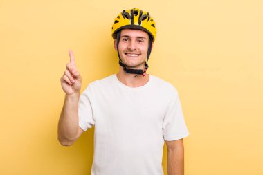 Genç yakışıklı adam gülümsüyor ve arkadaş canlısı görünüyor, bir numarayı gösteriyor. Bisiklet konsepti motor konsepti