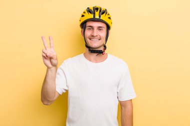 Genç yakışıklı adam gülümsüyor ve arkadaş canlısı görünüyor, iki numarayı gösteriyor. Bisiklet konsepti motor konsepti