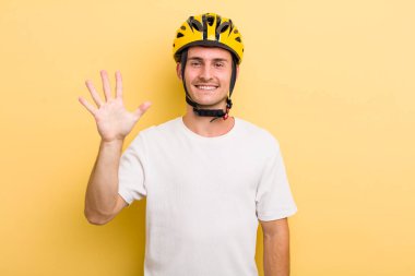 Genç yakışıklı adam gülümsüyor ve arkadaş canlısı görünüyor, beş numarayı gösteriyor. Bisiklet konsepti motor konsepti