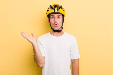 Genç, yakışıklı adam şaşırmış ve şok olmuş görünüyor. Çenesi düşmüş, elinde bir nesne var. Bisiklet konsepti motor konsepti