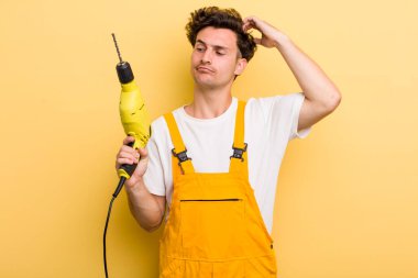 Genç yakışıklı adam mutlu bir şekilde gülümsüyor ve hayal kuruyor ya da şüphe ediyor. Matkap konsepti olan bir tamirci.