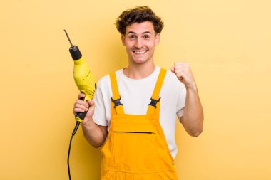 Genç yakışıklı adam şok olmuş hissediyor, gülüyor ve başarıyı kutluyor. Matkap konsepti olan bir tamirci.