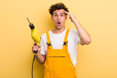 Genç yakışıklı adam mutlu, şaşkın ve şaşırmış görünüyor. Matkap konsepti olan bir tamirci.