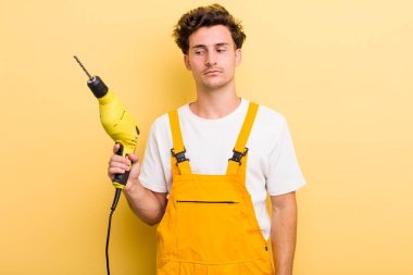 Genç yakışıklı adam üzgün, üzgün ya da kızgın hissediyor ve yana bakıyor. Matkap konsepti olan bir tamirci.