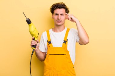 Genç yakışıklı, kafası karışık ve şaşkın hissediyor, sana deli olduğunu gösteriyor. Matkap konsepti olan bir tamirci.